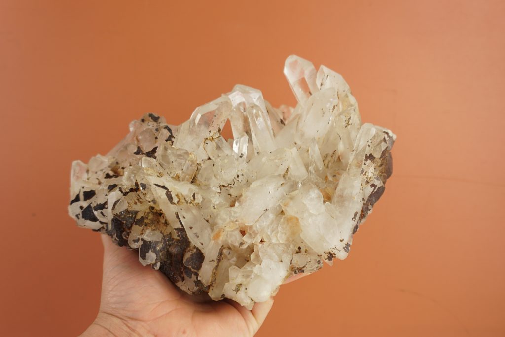Hand holding a large, dirty cluster of quartz with a lot of dark iron deposits