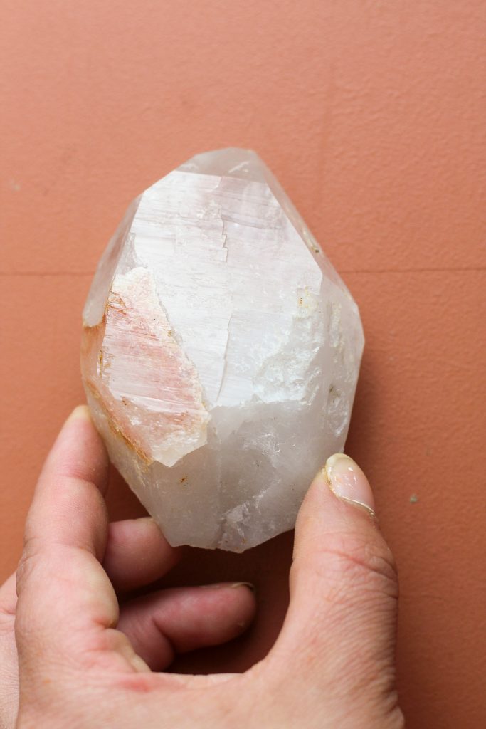 hand holding a palm sized quartz point with red staining